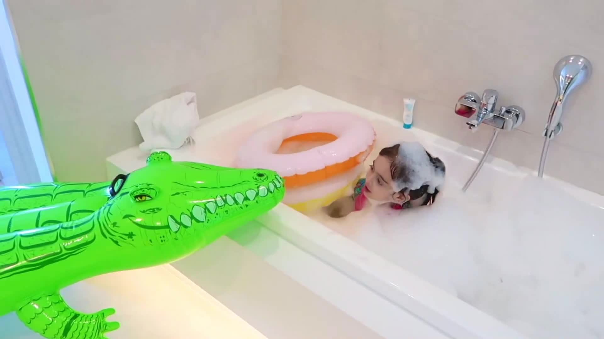 A little girl is having so much fun in the bathtub! There are lots of bubbles, a cute green inflatable crocodile toy, and colorful swim rings nearby. She's splashing, playing, and enjoying her bubble bath adventure—so playful and cozy! 🥰💦