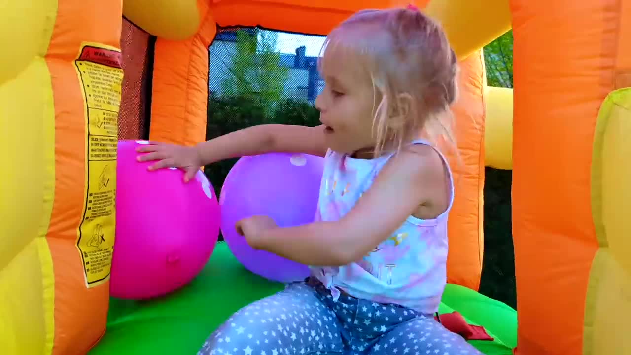 A cute little girl is having a blast in a colorful inflatable bouncy castle! She's playing with bright pink and purple balls, bouncing around and smiling the whole time. It's such a happy scene of kids' playtime joy! 😊🎾 #BouncyCastleFun #KidsPlayTime