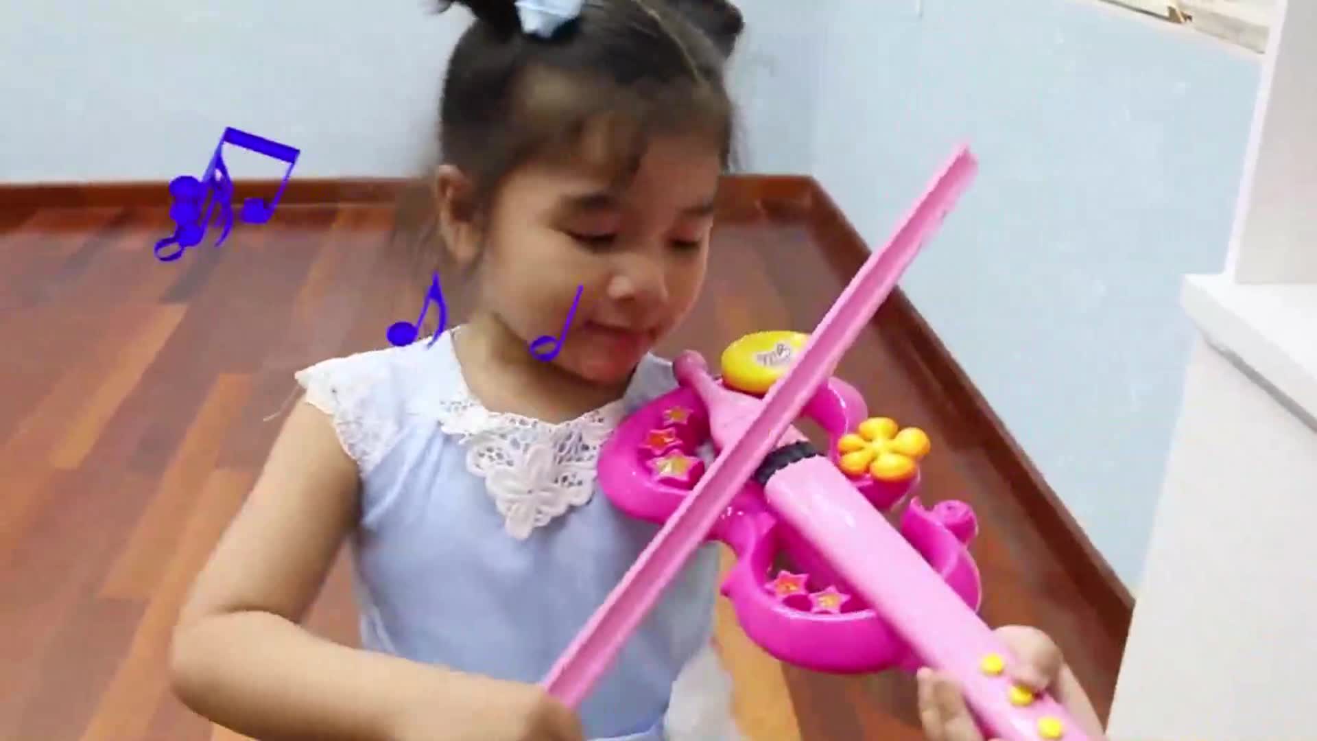 A sweet little girl is happily playing with her pink toy violin! She's moving the bow gently, making cheerful sounds, and there are cute musical notes floating around, looking so joyful and full of energy! 😊✨