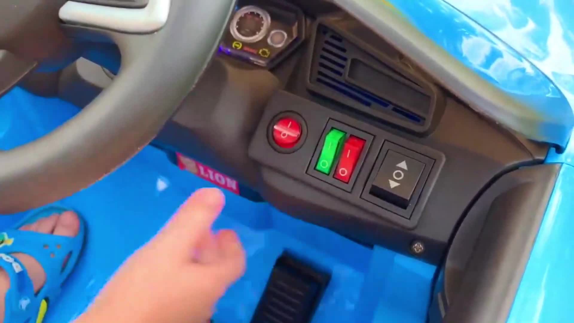 A cute little hand reaches for the toy car’s controls—turning the steering wheel, pressing the red and green buttons, and pretending to drive! It’s all about fun, adventure, and learning to ‘steer’ with this awesome toy car. 🚀🎮