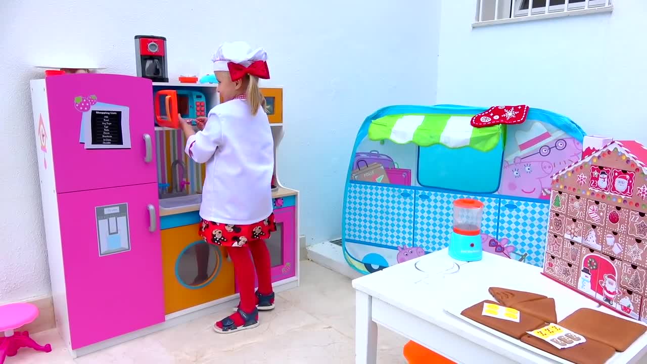 A little chef in a cute white coat and red bow is having a blast with her colorful play kitchen! 👩🍳 She’s pretending to cook, open the fridge, and use the coffee maker, while nearby, a Peppa Pig tent 🏠 and a fun gingerbread house calendar 🍪 add to the playful scene! It’s all about imagination and making delicious toy treats—perfect for little cooks! 🎉