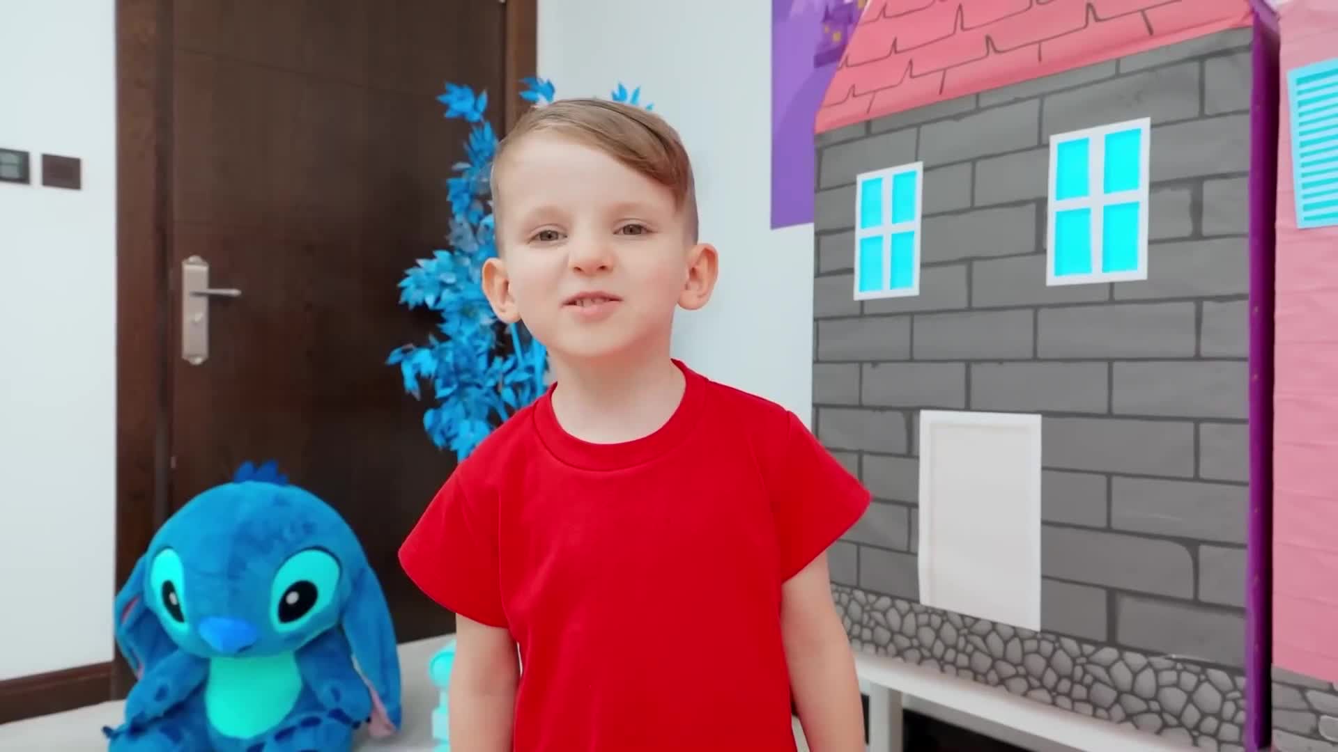 A cute little boy in a red shirt plays with his blue Stitch stuffed friend in a colorful room with a toy house! They're having so much fun—maybe they're going on a pretend adventure together? 🧸✨ Perfect for playtime inspiration! Watch and smile! 😊