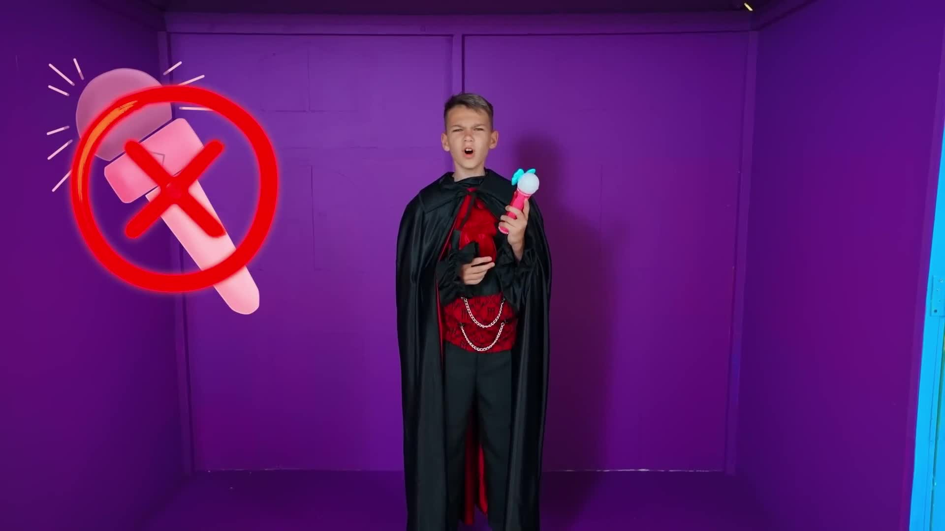 A tiny vampire in a black cape 🧛♂️ grabs his sparkly toy mic, but a big red X says 'no singing!' 🎤🚫 Watch if he finds a spooky way to perform anyway! 😱✨